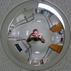 a man is taking a selfie with his camera in an office building's circular mirror