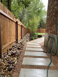 a stone path in front of a wooden fence with water hoses attached to it