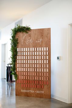 a wooden sign with the names and date on it in front of a wall decorated with greenery