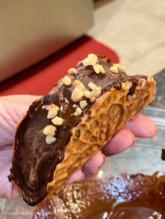 a hand holding a half eaten chocolate covered doughnut with nuts on it's side