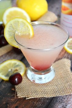 a drink in a glass with lemons and cherries around it on a wooden table