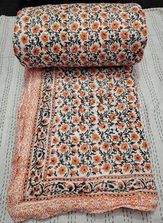 an orange and black flowered blanket laying on top of a white tablecloth with stripes