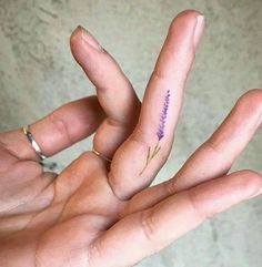 a person's hand holding a tiny purple flower tattoo on their left index finger