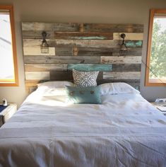 a bed with white sheets and pillows in a bedroom next to two windows that have wood planks on them