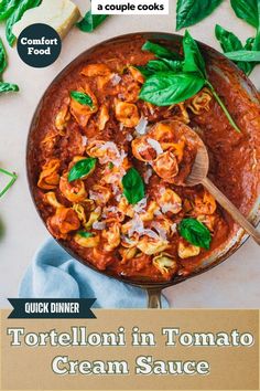 a pan filled with tortellini in tomato cream sauce and spinach leaves on the side