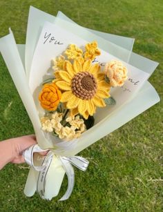 a hand holding a bouquet of flowers on top of a green grass covered park area