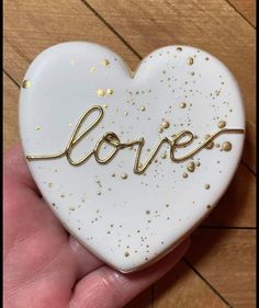 a hand holding a white and gold heart with the word love spelled in cursive writing