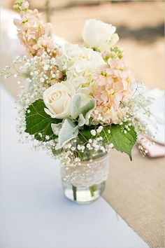 a vase filled with white and pink flowers sitting on top of a blue table cloth