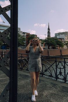 a woman walking across a bridge while talking on a cell phone with buildings in the background