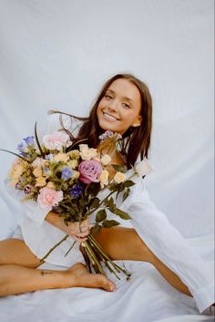 a woman sitting on the floor holding a bouquet of flowers in her hands and smiling