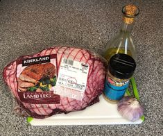 raw meat, garlic and seasoning on a cutting board next to a bottle of wine