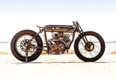 an old fashioned motorcycle is parked on the sand by the water's edge with no people around it