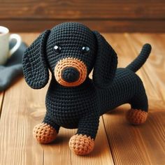 a crocheted black dog sitting on top of a wooden floor next to a cup