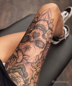 a woman's leg with a skull and flowers tattoo on her arm, sitting in a chair