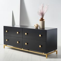 a black dresser with gold handles and drawers next to a potted plant on top