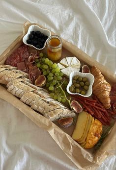 a tray with bread, olives, meat and cheese on it sitting on a white sheet