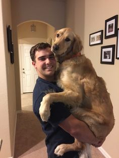 a man holding a large brown dog in his arms and smiling at the camera while standing next to a doorway