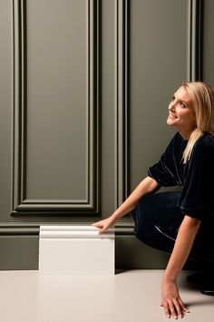 a woman sitting on the ground next to a white box with her hands out and looking up