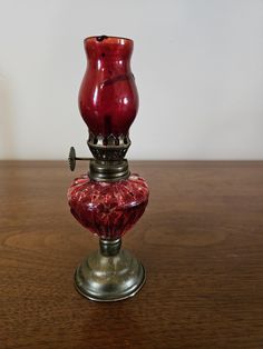 a red glass vase sitting on top of a wooden table next to a metal object