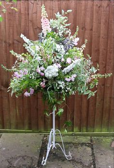 a bunch of flowers that are sitting on a stand in front of a wooden fence