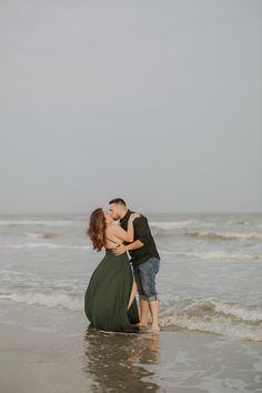 a man and woman kissing on the beach in front of the ocean while holding each other