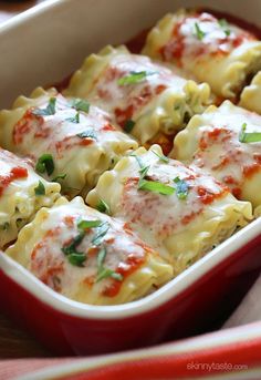 a red casserole dish filled with pasta and meat covered in sauce, cheese and parsley