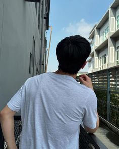 a man standing on the side of a building talking on a cell phone while wearing a white t - shirt