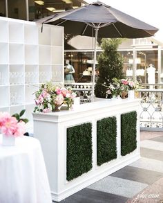 an outdoor bar with flowers and plants on the outside, next to a white table