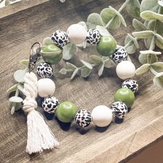 a green and white beaded bracelet with tassels on a wooden table next to plants