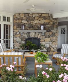 a stone fireplace in the middle of a patio surrounded by flowers and chairs with cushions on them