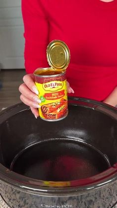 a woman is holding a can of canned food in her hand while standing next to an empty pot