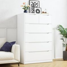 a white chest of drawers sitting in a living room next to a chair and potted plant