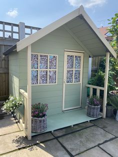 a small shed with some plants in the front yard and windows on the side wall