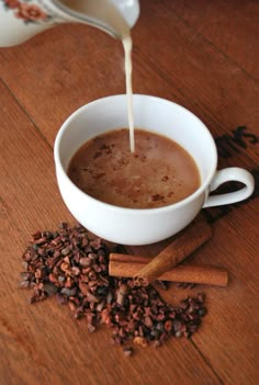 coffee being poured into a white cup with cinnamons on the table next to it