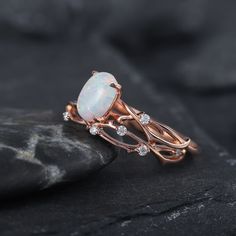 an opal and diamond ring sitting on top of a black rock with white stones