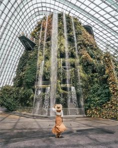 a woman is standing in front of a waterfall at gardens by the bay, singapore