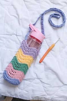 a crocheted water bottle with a straw in it next to a knitting needle