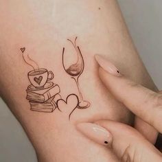 a woman's arm with a wine glass and books tattoo on it