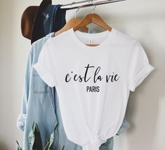 "This t-shirt is everything you've dreamed of and more. It feels soft and lightweight, with the right amount of stretch. It's comfortable and flattering for both men and women. C'est la Vie T-shirt | C'est la Vie Tee | France Shirt | French Shirt | Cest la Vie Paris Shirt H O W - T O - O R D E R - Be sure to review the size chart in the photos before making your selection.  - Select your size, color & quantity from the drop-down menus. - Click the \"Add to Cart\" button, then proceed to check ou Flower Girl Shirts, Drunk In Love, Bachelorette Party Shirts, Jesus Shirts, Mama Shirt, Party Shirts, Teacher Shirts, Mom Shirts, Namaste