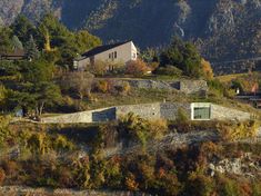 the house sits on top of a hill with trees around it and mountains in the background