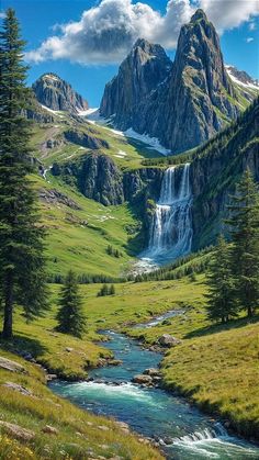 a stream running through a lush green valley next to tall mountain covered in snow and grass