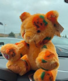 a teddy bear with orange and green paint on it's face sitting in the front seat of a car