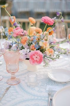 an arrangement of flowers in a vase on a table with plates and utensils