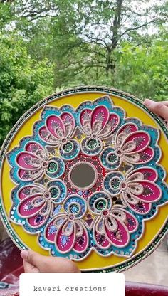 a person holding a yellow plate with colorful designs on it and trees in the background