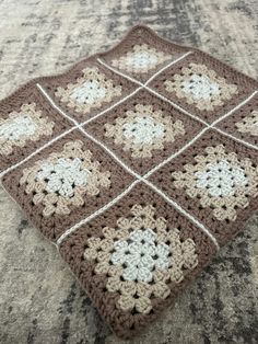 a brown and white crocheted blanket sitting on top of a carpet