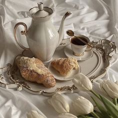 two croissants on a plate next to a tea pot