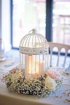 a birdcage filled with flowers on top of a table next to a candle