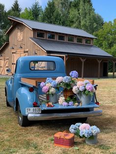 an old blue truck with flowers on the back parked in front of a wooden barn