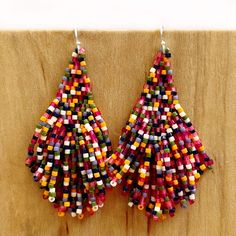 two pairs of multicolored beaded earrings hanging from hooks on a wooden board