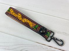 a leather key chain with sunflowers painted on the front and sides, hanging from a hook